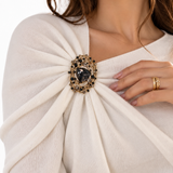 Broche Catarina dourado com pedras escuras sobre blusa clara