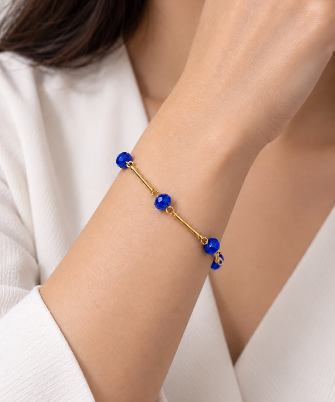 Pulseira dourada com contas azuis e pingente na extremidade