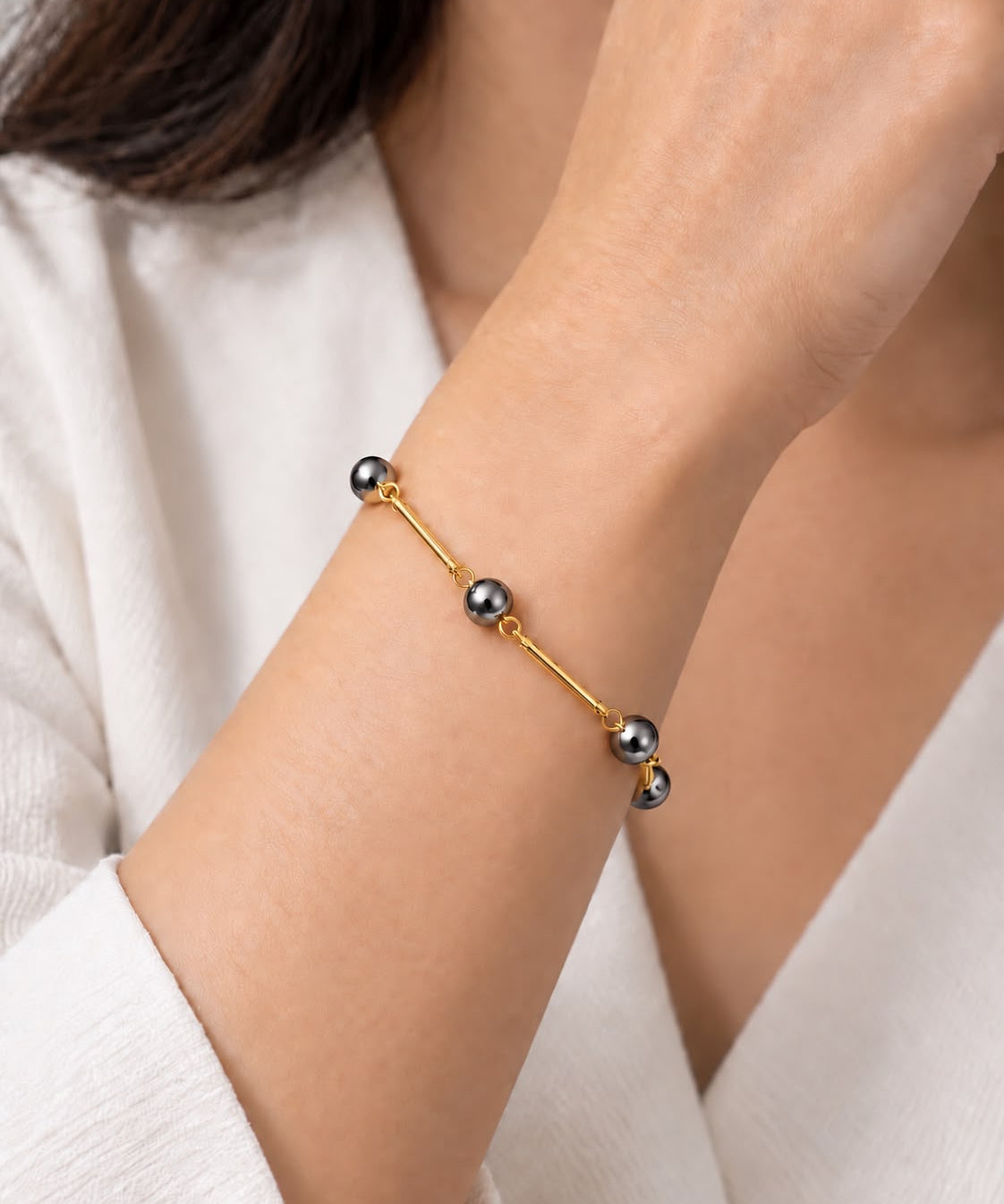 Pulseira Ana Célia Ônix dourada com esferas de ônix escuras no pulso