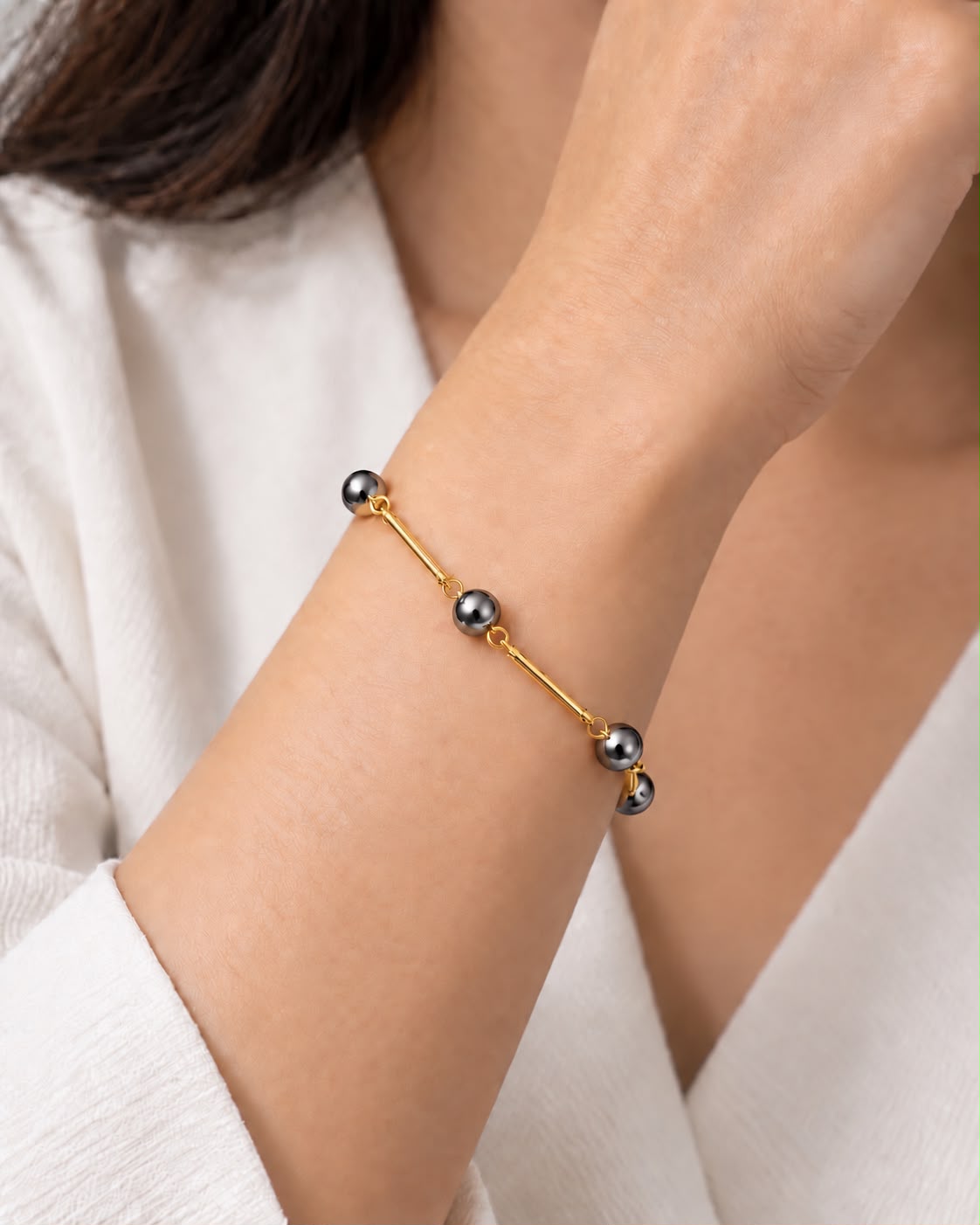 Pulseira Ana Célia Ônix dourada com esferas de ônix escuras no pulso