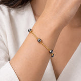 Pulseira Ana Célia Ônix dourada com esferas de ônix escuras no pulso
