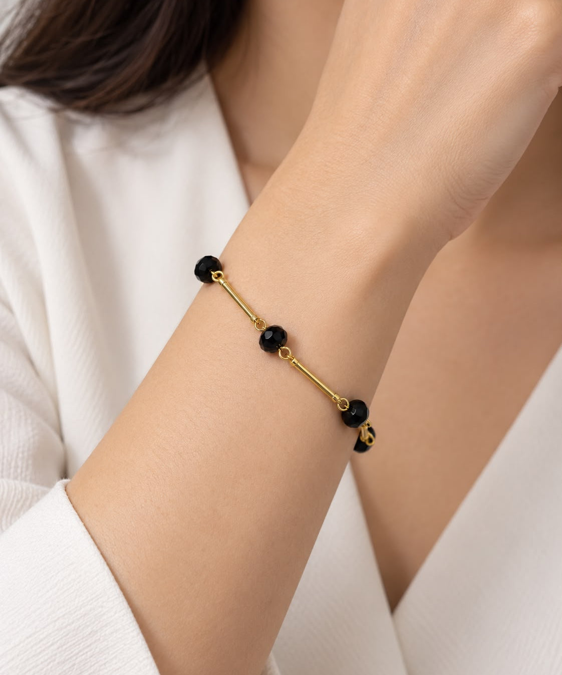 Pulseira preta com contas e fecho dourado, elos finos e detalhes arredondados