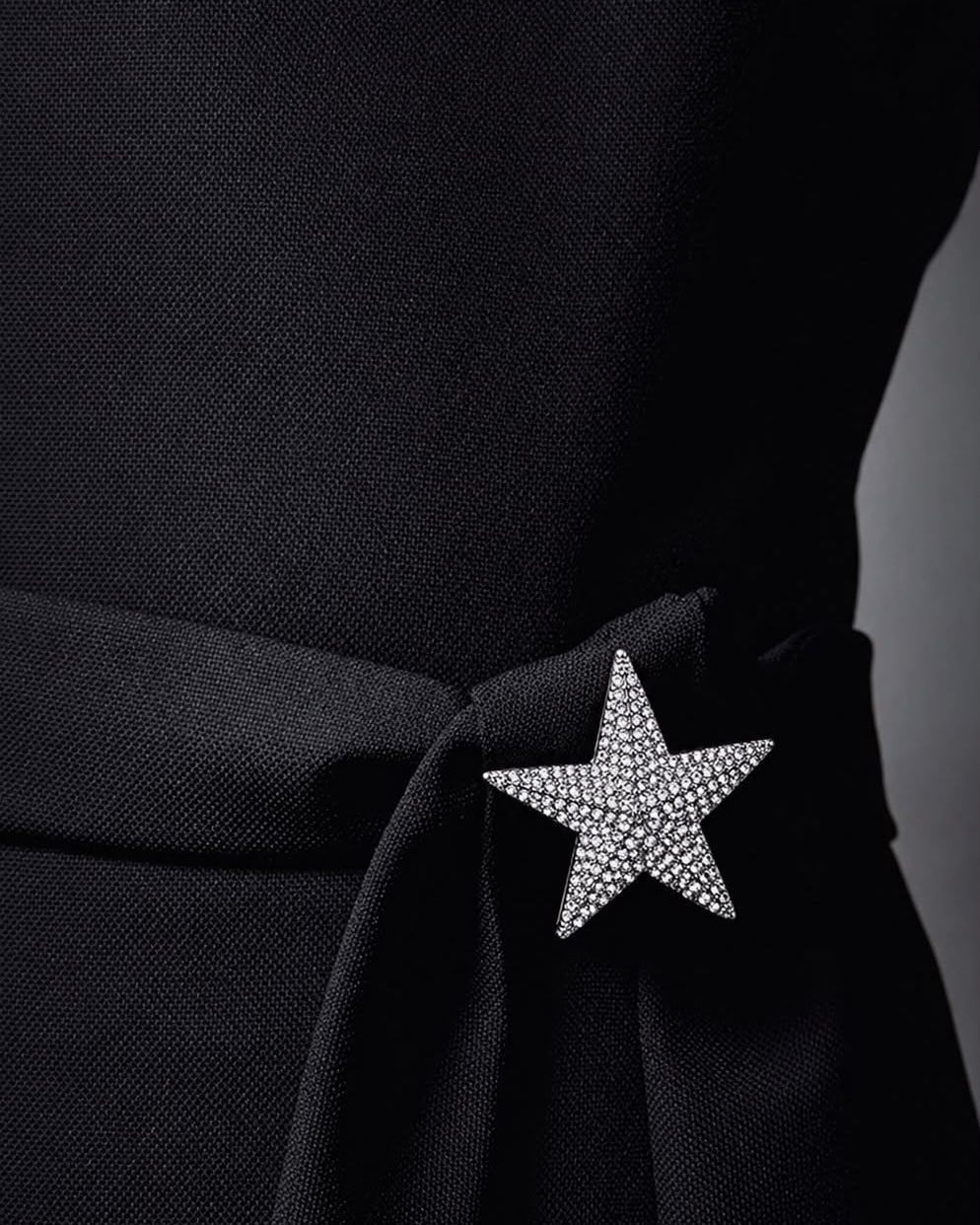 Broche de estrela com cristais prateados, preso ao tecido escuro.