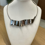 Colar prateado com franja de placas retangulares, fecho lateral.