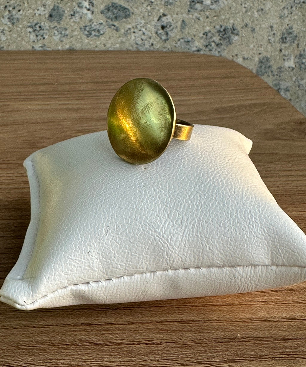 Anel oval dourado brilhante com pedra verde e aro dourado.