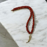 Colar de contas vermelho com pingente de chifre dourado e fecho metálico