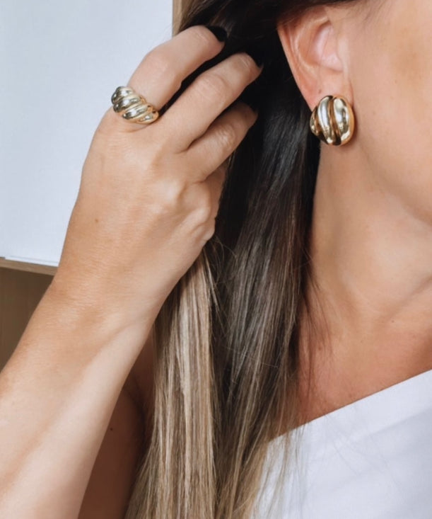 Anel Lucinda dourado com pedra escura e detalhes metálicos no dedo