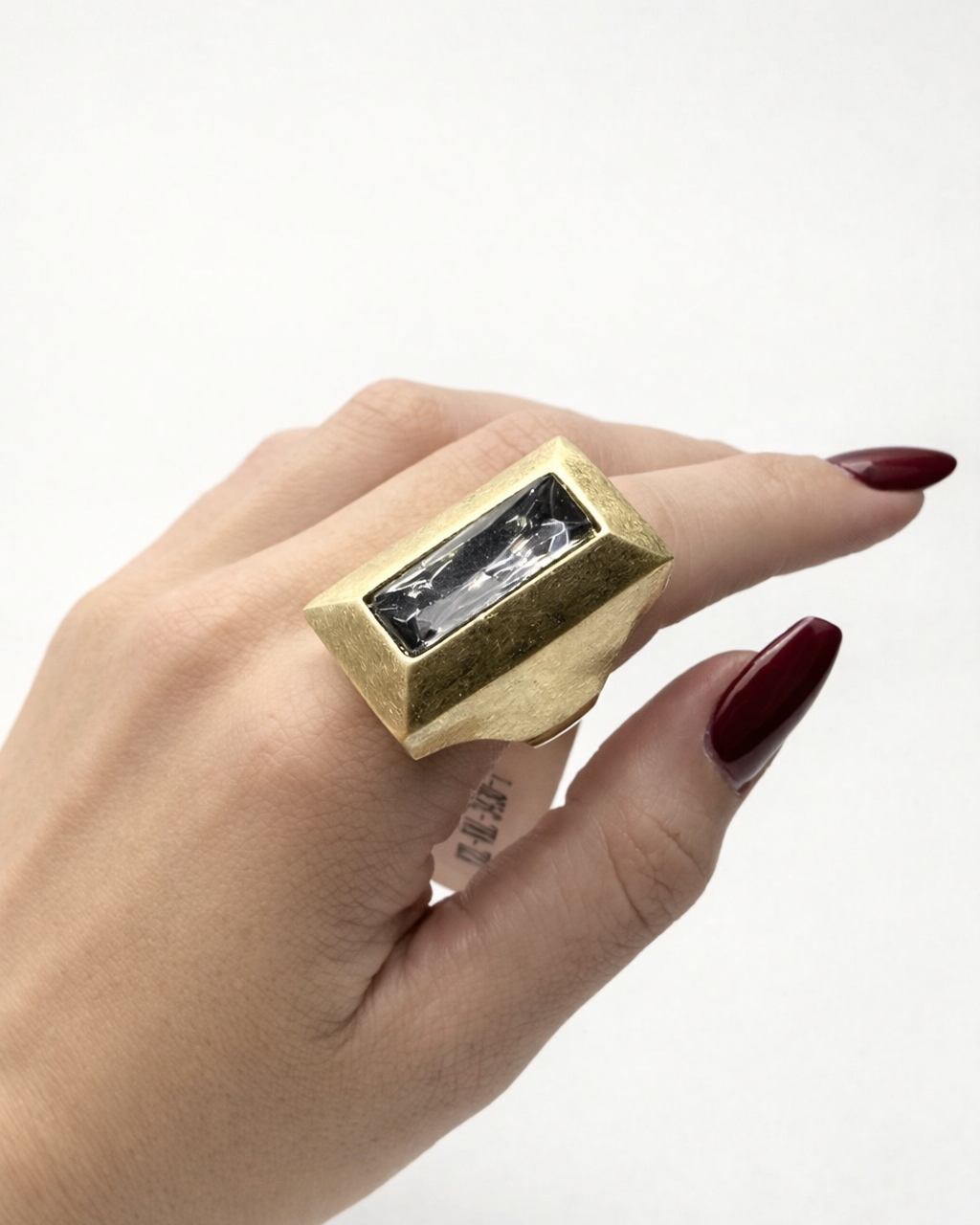 Anel retangular dourado com pedra transparente no dedo, acabamento texturizado