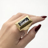 Anel retangular dourado com pedra transparente no dedo, acabamento texturizado