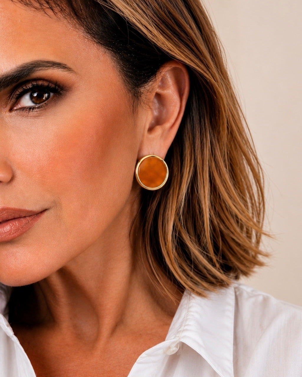 Brinco Tula redondo com aro dourado e disco âmbar, usado na orelha
