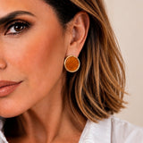Brinco Tula redondo com aro dourado e disco âmbar, usado na orelha