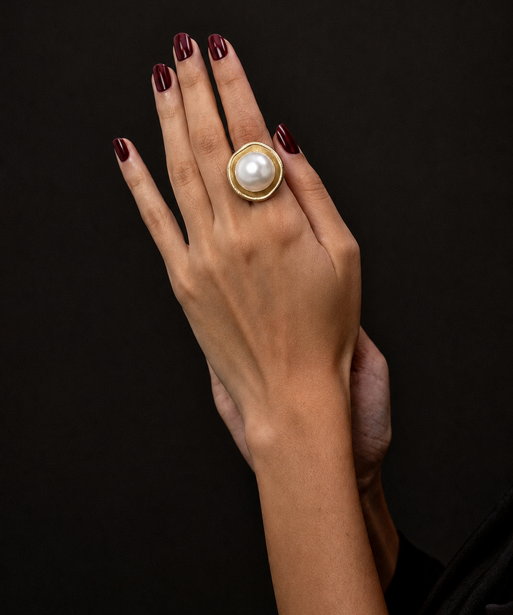 Anel Maiorca dourado com pérola branca; anel na mão com esmalte escuro