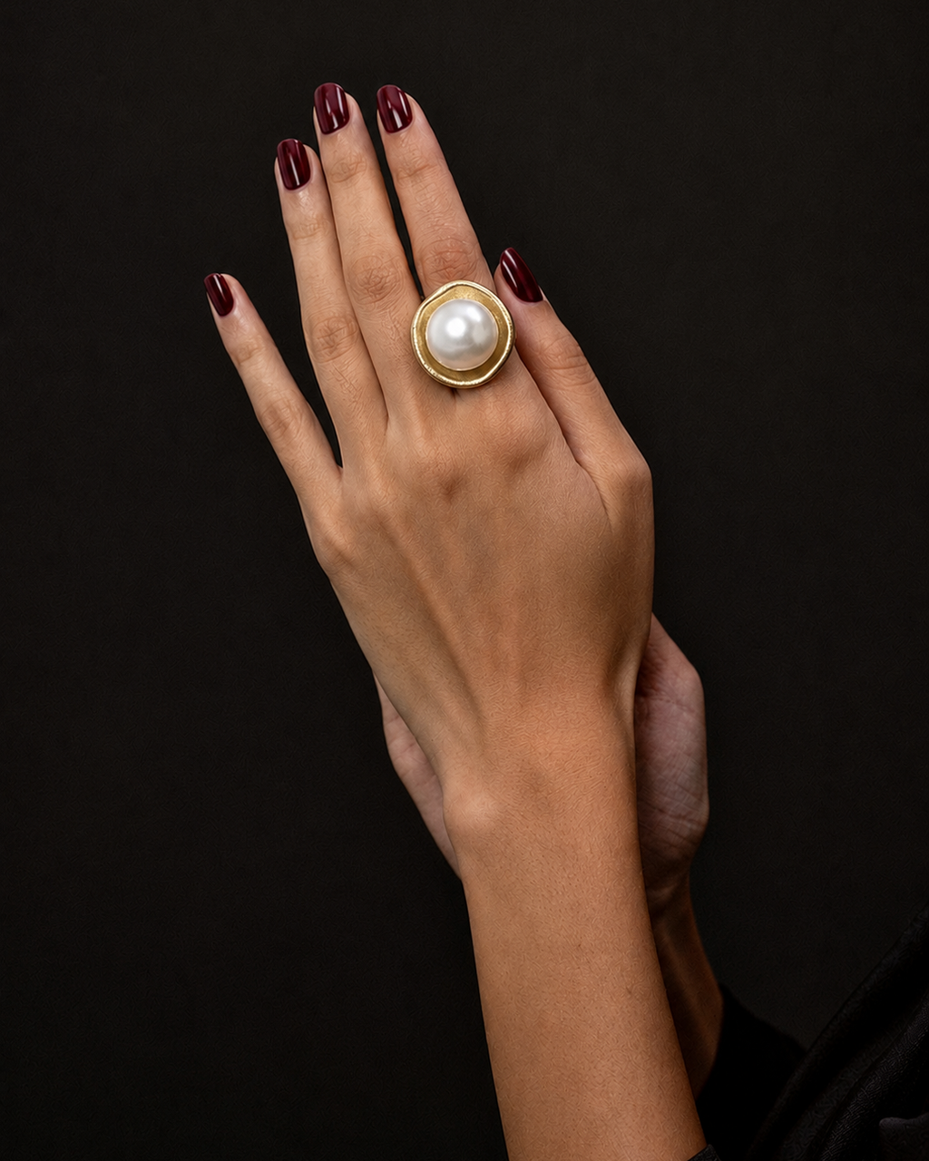 Anel Maiorca dourado com pérola branca; anel na mão com esmalte escuro