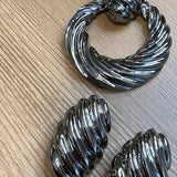 Par de brincos de argola metálicos ovalados, com textura ondulada e acabamento prateado