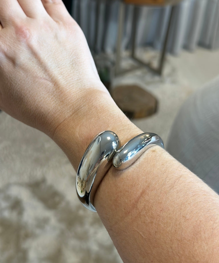 Pulseira prateada de elos curvos no pulso.