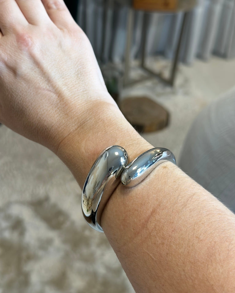 Pulseira prateada de elos curvos no pulso.