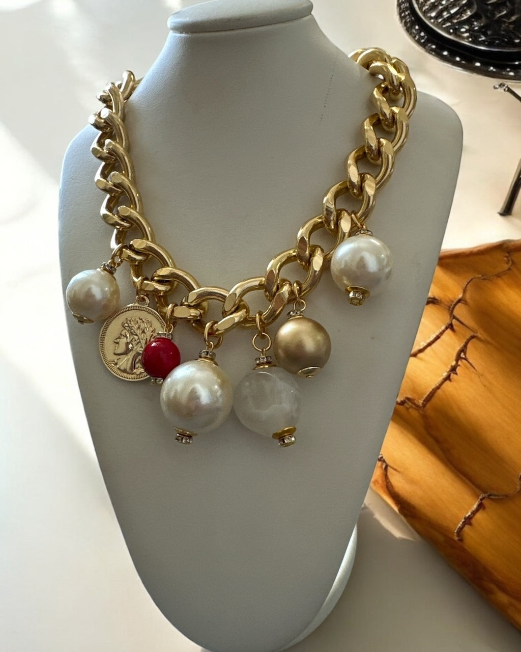 Colar dourado com correntes grossas, pérolas e pingentes com detalhe vermelho