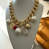 Colar dourado com correntes grossas, pérolas e pingentes com detalhe vermelho