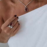 Anel prateado com pedra vermelha oval e detalhes em metal