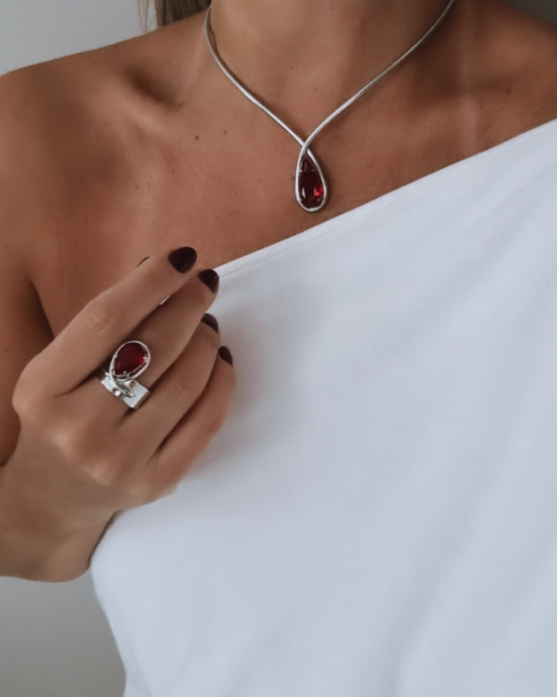 Anel prateado com pedra vermelha oval e detalhes em metal