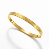 Pulseira Carti de listras douradas, aro fino com padrão gravado e brilho metálico.