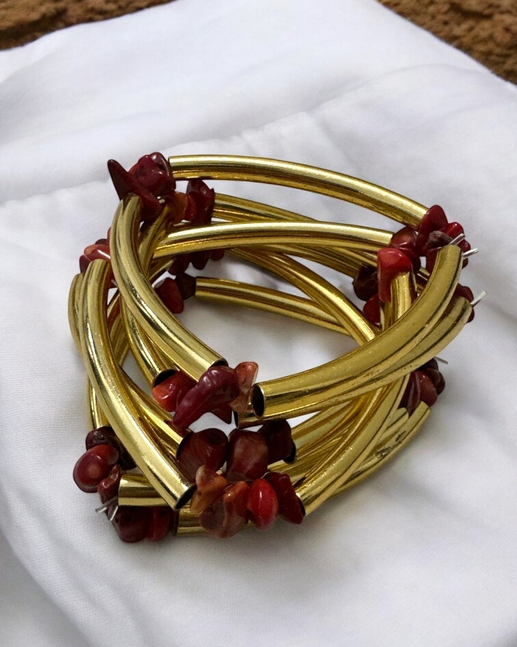 Pulseira dourada com pedras vermelhas e hastes trançadas