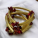Pulseira dourada com pedras vermelhas e hastes trançadas