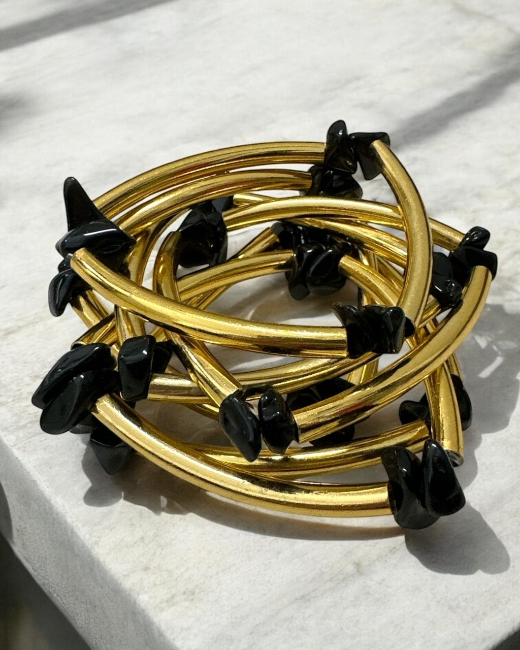 Pulseira dourada com pedras pretas em hastes trançadas