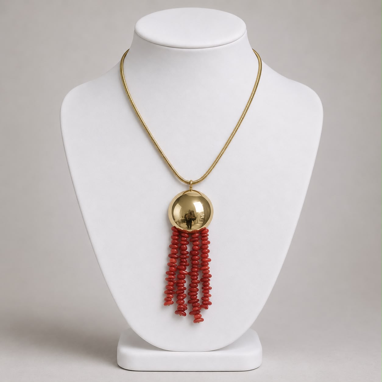 Colar dourado com pingente redondo e franjas de miçangas vermelhas, na gola