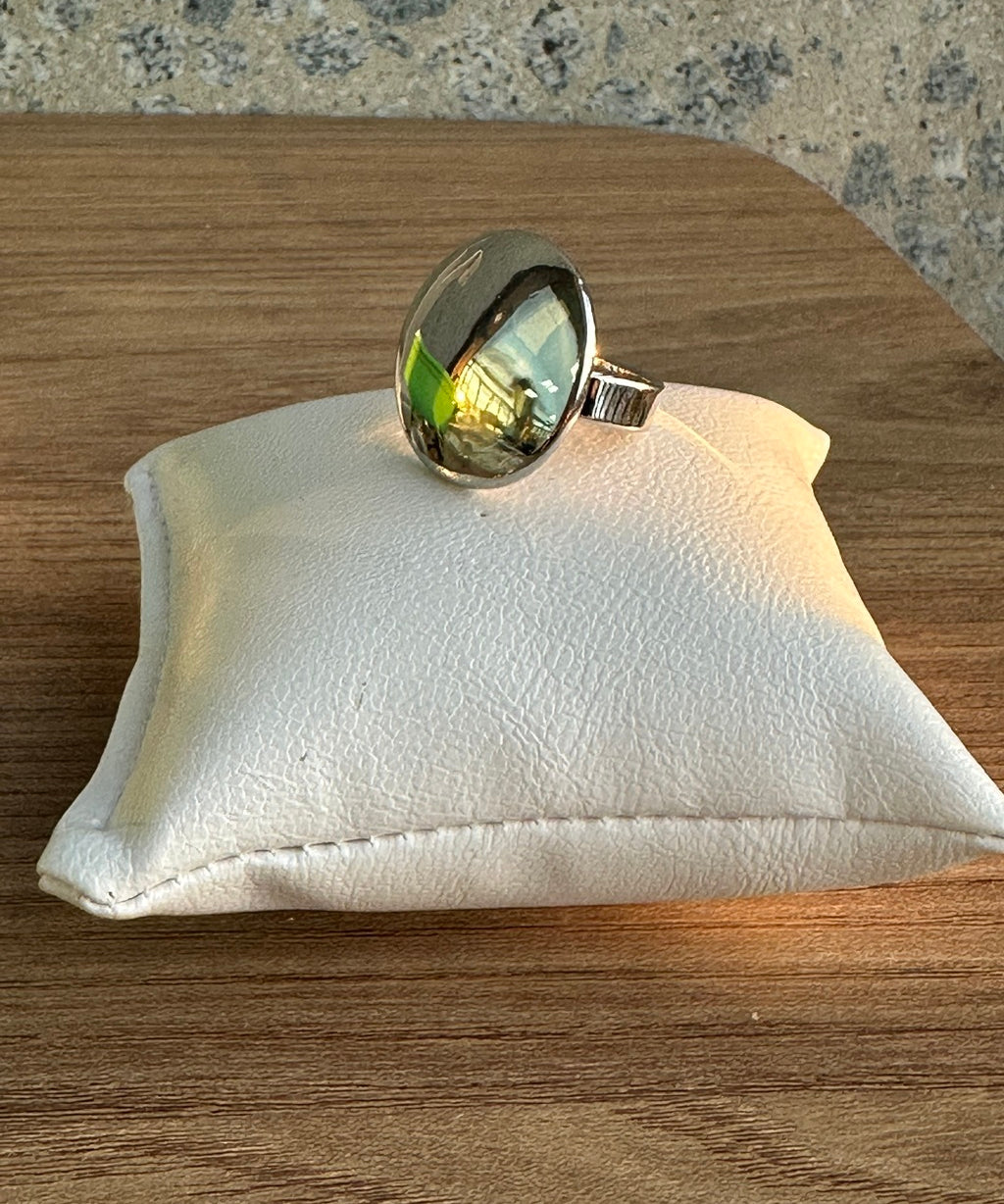 Anel oval verde com moldura dourada e aro prateado.