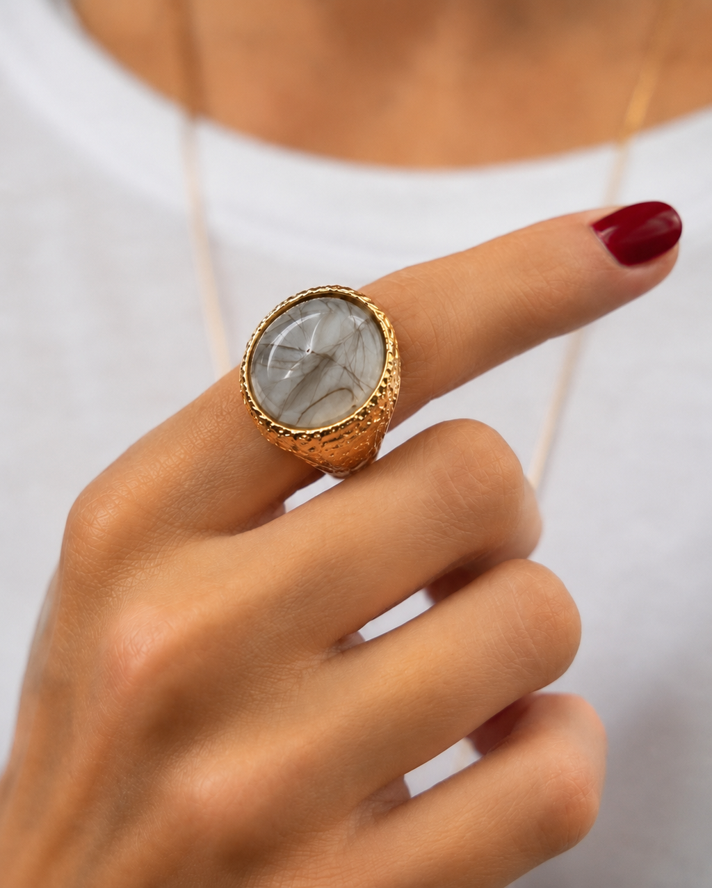 Anel dourado com pedra oval transparente com veios, usado em mão