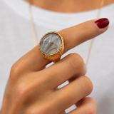 Anel dourado com pedra oval transparente com veios, usado em mão
