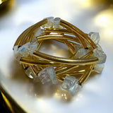 Pulseira dourada com pedras transparentes quadradas e hastes trançadas